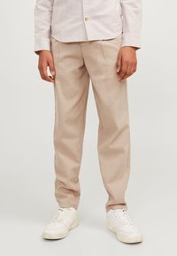 Beige linnebyxor med lös passform, med framviks. Matchas med vita sneakers. Bakgrunden är neutral och diskret.