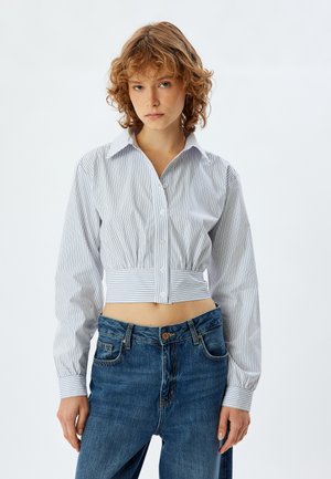 Camicia abbottonata tagliata in azzurro chiaro con righe bianche, caratterizzata da un colletto classico e maniche lunghe. Abbinata a jeans a vita alta.