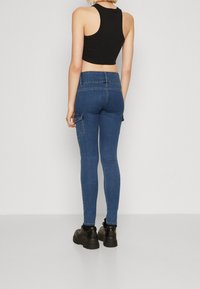 Jeans skinny de denim azul con bolsillos tipo cargo, ligeramente elásticos y de talle medio. Combinados con un top corto negro y zapatos chunky negros.