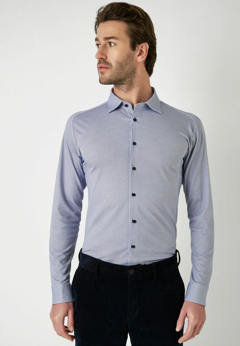 Himmelblaues Hemd mit Knöpfen, gemusterter Textur, langen Ärmeln und schwarzen Knöpfen, kombiniert mit dunklen Hosen.