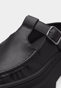 Μαύρο δερμάτινο σανδάλι με ασημένιο λουρί με αγκράφα και πλευρική κοπή σε παχιά ελαστική σόλα.