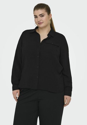 Camicia nera a maniche lunghe con bottoni e tasca sul petto, caratterizzata da un design testurizzato e una vestibilità rilassata, abbinata a pantaloni neri larghi.