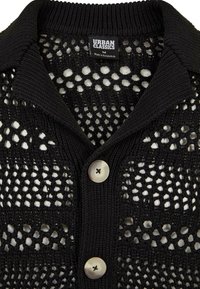 Černý volně pletený kardigan s velkým límcem a dvěma světle zbarvenými knoflíky, s viditelnou značkou Urban Classics a štítkem velikosti střední.