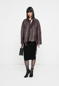 Burgundy leather biker jacket with silver hardware, paired with a black patterned skirt and sheer black tights. Black handbag and heels complete the look.