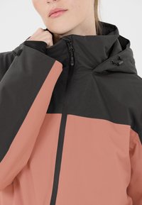 Wasserdichte Jacke in Schwarz und Rosarot. Sie verfügt über einen hohen Kragen, einen Reißverschluss und eine verstellbare Kapuze mit Kordelzug sowie eine glatte Textur.