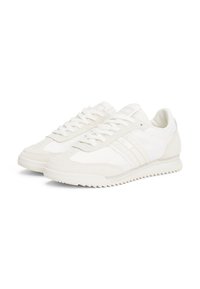 Une paire de baskets basses ivoire avec des accents en daim, fermeture à lacets et semelles en caoutchouc texturé, présentée sur un fond blanc.