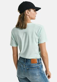 Mintgrøn t-shirt med korte ærmer og afslappet pasform, parret med højtaljede blå jeans med en brun læderlap på bagsiden.