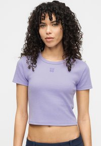 Ανοιχτό μωβ κοντομάνικο crop top κατασκευασμένο από απαλό ύφασμα. Διαθέτει κοντά μανίκια και στρογγυλή λαιμόκοψη με κεντημένο λογότυπο "HUGO" στο στήθος.