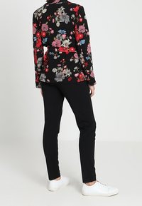 Květinová blůza v černé barvě s červenými, růžovými a modrými květinami, v kombinaci s černými kalhotami a bílými teniskami. Blůza má límeček a dlouhé rukávy.