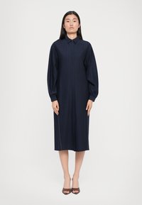 Marineblå midi-kjole med vertikale striper, klassisk krage, puffede ermer og rett snitt. Stoffet ser glatt ut med en subtil glans.
