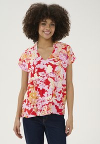 Cvetna bluzica s kratkimi rokavi z V-izrezom, živahne rdeče barve, z mešanico rožnatih in rumenih cvetličnih vzorcev na mehkem materialu.