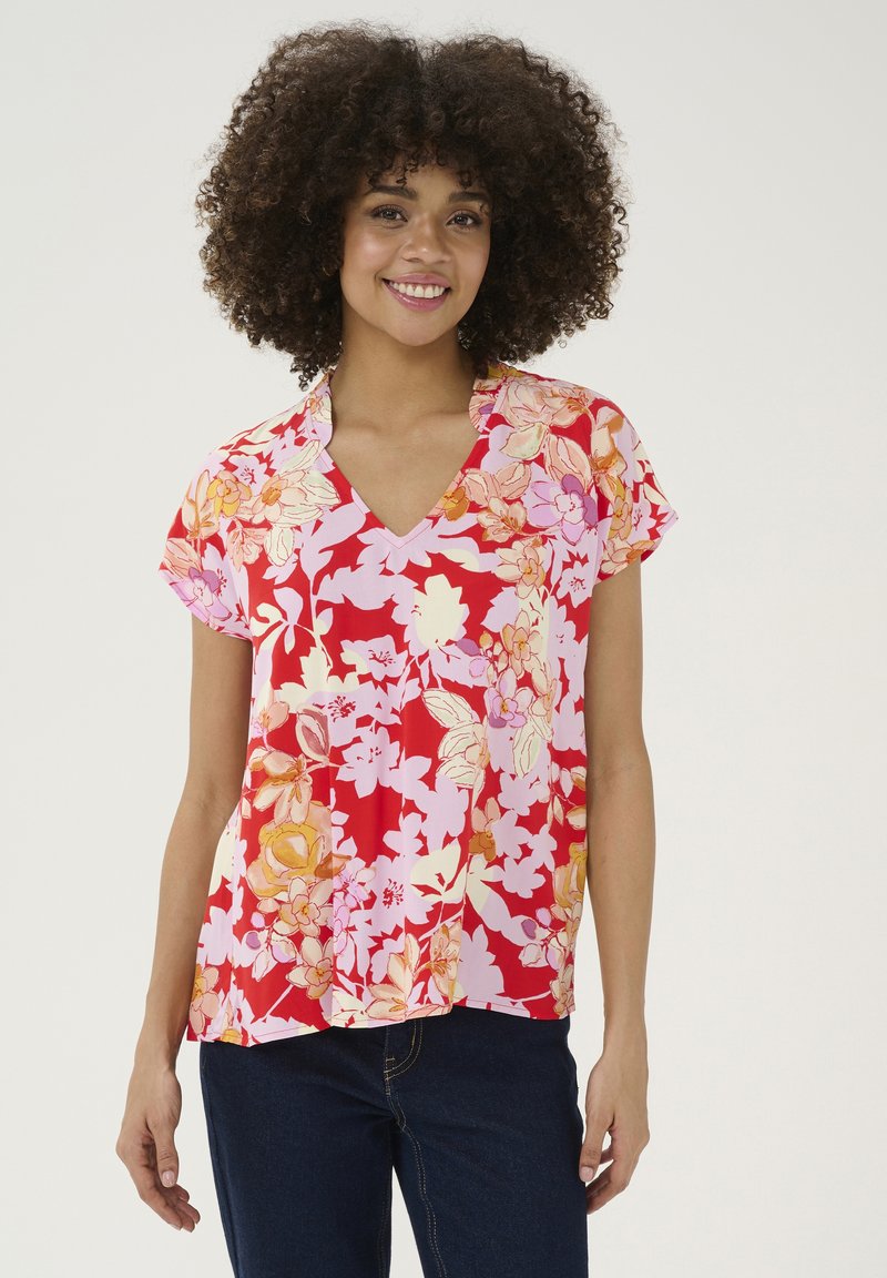 Cvetna bluzica s kratkimi rokavi z V-izrezom, živahne rdeče barve, z mešanico rožnatih in rumenih cvetličnih vzorcev na mehkem materialu.