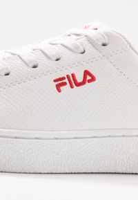 Sneaker bianca in pelle con superficie testurizzata, dotata di suola bianca anch'essa testurizzata e logo ricamato "FILA" rosso sul lato.