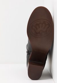 Chaussure en cuir noir avec un bout arrondi et un talon en caoutchouc marron. Présente une semelle texturée et des détails de coutures subtiles sur les côtés.