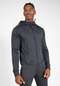 Donkergrijze zip-up hoodie met een rits aan de voorkant, twee zijzakken en een hoodie met trekkoord. Gemaakt van glad, lichtgewicht stof.