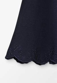 Námorně modrá látka s texturovaným povrchem, s vykrojeným okrajem a květinovou výšivkou na lemu.