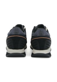 Par de zapatillas negras y grises con una franja naranja, vistas desde atrás, mostrando cuellos acolchados en el talón y mediasoles blancos.