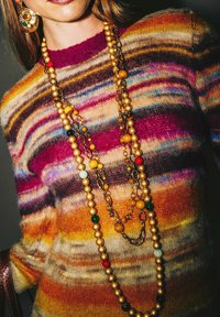 Mehrfarbiger gestreifter Pullover aus Wollmischung mit goldenem Schmuck, der bunte Perlen und Kettenakzente zeigt. Reichhaltige Texturen und lebendige Farbtöne.