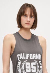Sivi majica bez rukava od pamuka s okruglim izrezom. Sadrži bijeli grafički natpis "CALIFORNIA 95" i laurelske akcenta.