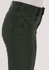 Donkergroene skinny jeans met een gladde textuur, voorzien van achterzakken en een aansluitend ontwerp. Geen zichtbare hardware of patronen.