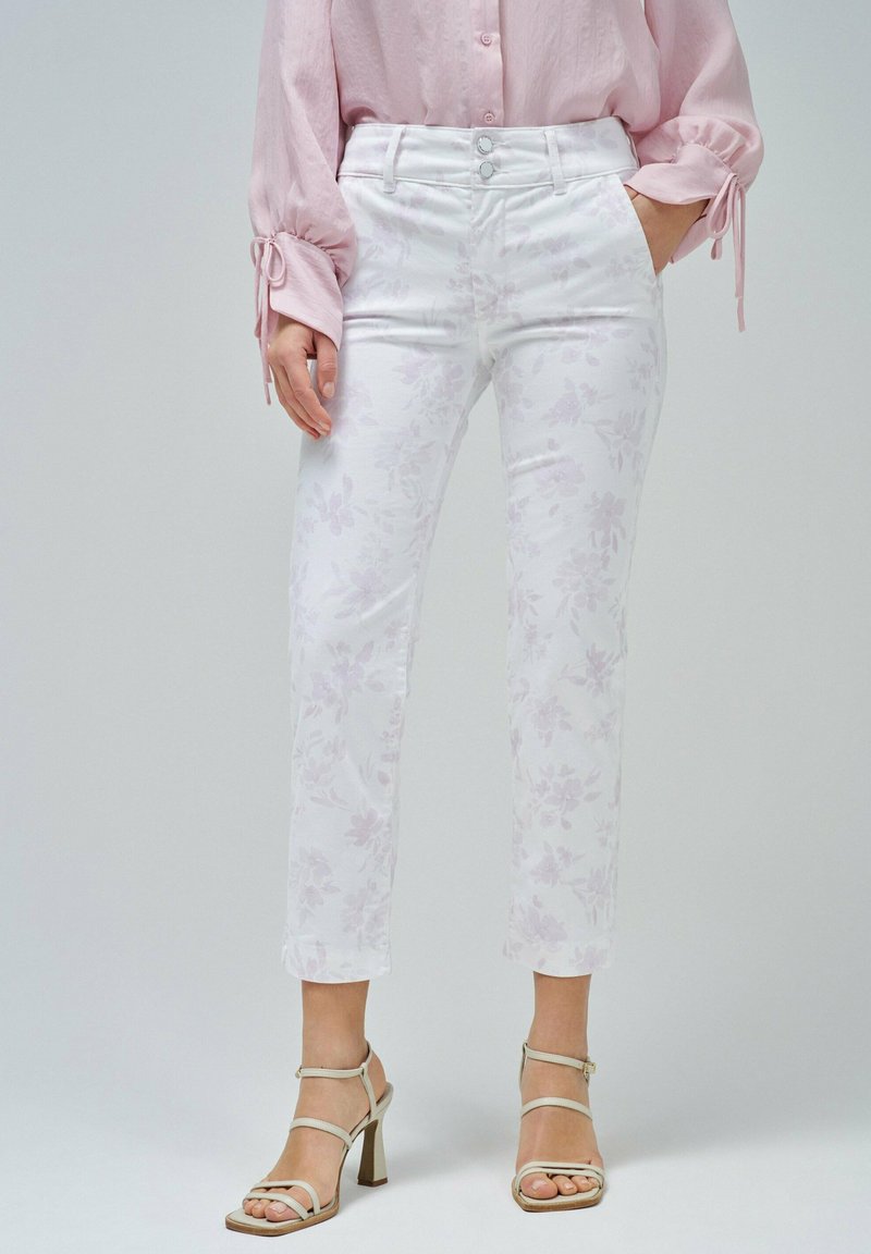 Pantalones ajustados de patrón floral blanco con un diseño de cinco bolsillos, combinados con una camisa de botón color rosa claro y tacones de tiras beige.
