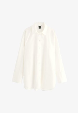 Vit långärmad skjorta med knappstängning, krage, raka manschetter och något rundad nederkant, visad liggande mot en vit bakgrund.