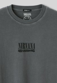 T-shirt en coton gris avec col rond, imprimé sur le devant avec le texte noir "NIRVANA" et "NEVERMIND". Texture douce et design ample.
