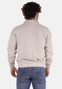 Giacca di corduroy beige chiaro con colletto alto e polsini elasticizzati, caratterizzata da una trama semplice e una vestibilità rilassata, vista da dietro.