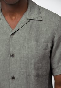 Grijze korte mouwen shirt van textuurstof, met een opstaande kraag, drie knopen en een patchzak aan de linkerkant.
