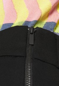 Färgglad mönstrad tyg övergår till en enhetlig svart del med en smidig dragkedja. Textilen har nyanser av rosa, gult och blått.