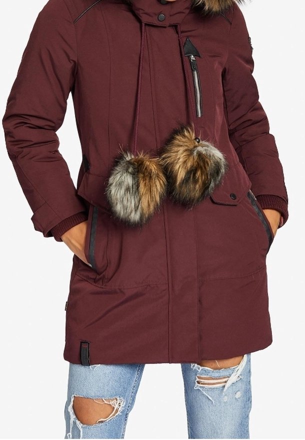 Parka burdeos con capucha, con detalles de pompón de piel, bolsillo con cremallera y puños de canalé. Llevado sobre jeans de denim desgastados.