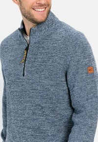 Blauer Strickpullover mit Reißverschlusskragen, aus strukturierter Stoff gefertigt und mit einem Lederakzent am linken Ärmel.