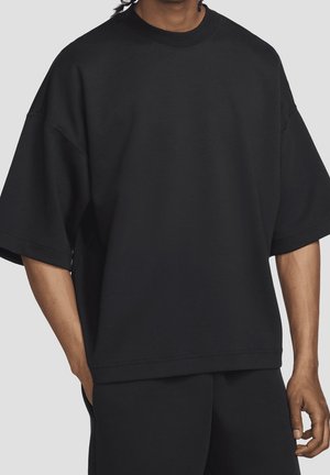 Schwarzes übergroßes Sweatshirt mit kurzen Ärmeln und Rundhalsausschnitt, aus weichem, strukturiertem Stoff, mit lockerem Schnitt und minimalen Nahtdetails.