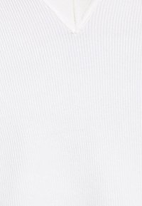 Pull en maille côtelée blanche avec un col en V et une texture douce. Le tissu présente de fines lignes verticales.