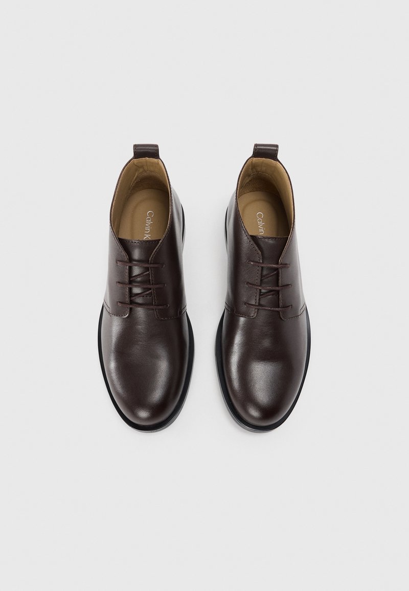 Bottines en cuir marron avec une finition lisse, bout rond, design à lacets et semelle en caoutchouc noir, avec un petit talon.