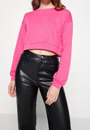 Felpa fucsia corta con maniche lunghe e polsini a coste, abbinata a pantaloni neri in ecopelle a vita alta con chiusura a bottone.