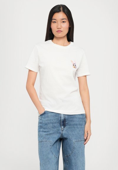 White cotton t-shirt with short sleeves, round neckline, and a colorful embroidered bunny design on the left chest. Blue denim jeans are worn.