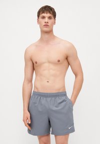 Shorts de sport gris avec une taille élastique, des poches latérales et un logo Nike blanc en bas à gauche à l'avant. Tissu lisse et léger.