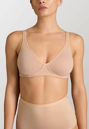 Donna che indossa un reggiseno senza cuciture color nudo e mutandine a vita alta abbinate su uno sfondo chiaro.