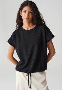 Zwarte top met korte mouwen, voorzien van een gestructureerd patroon, ronde halslijn en een verstelbare strik aan de onderkant. Verhoogd casual ontwerp in een zachte stof.