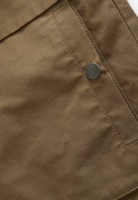 Gros plan sur un tissu marron avec une poche cousue et un bouton en métal texturé gravé de "EST. 1962."