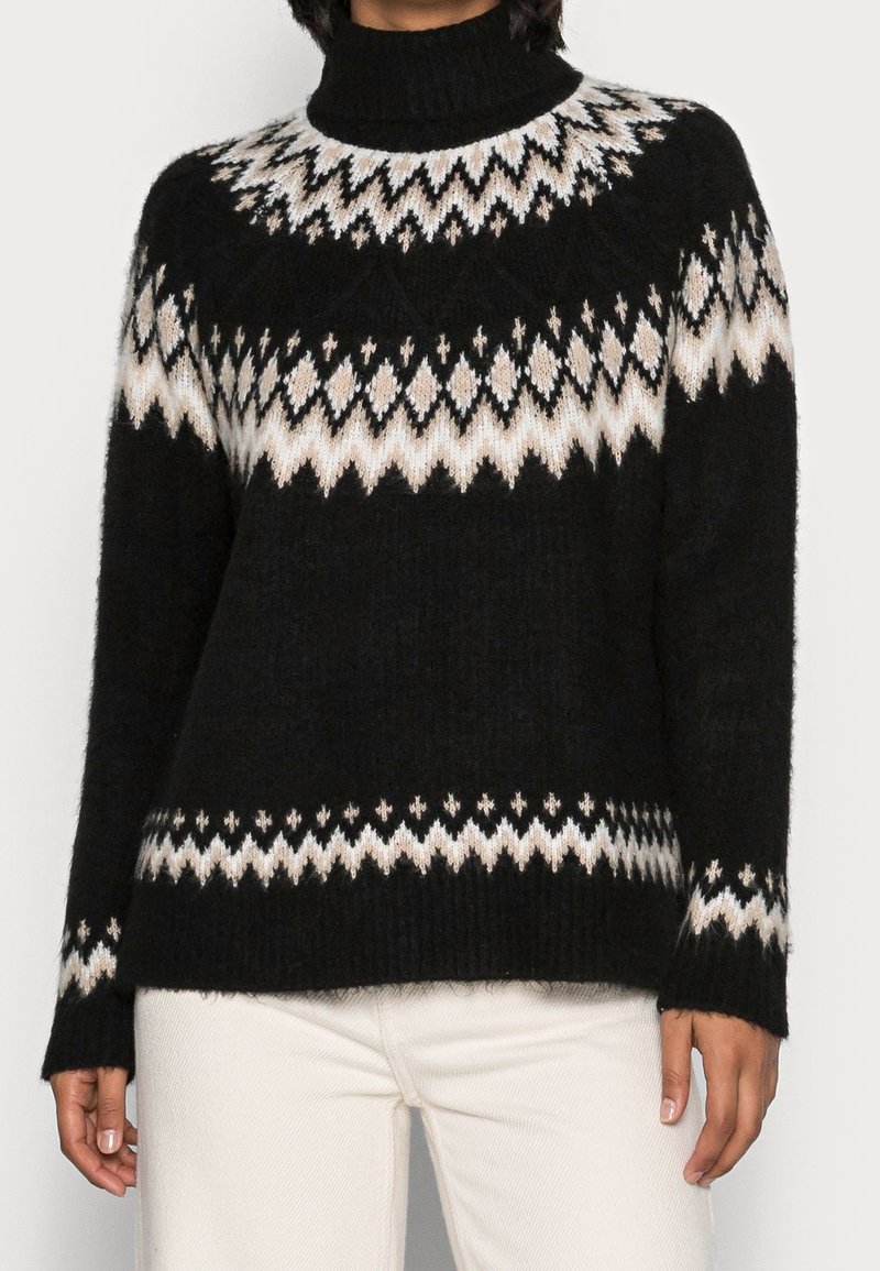 Schwarzer Strickpullover mit hohem Kragen, der ein weißes und beiges geometrisches Muster auf der Brust und den Ärmeln aufweist. Weiche Textur.