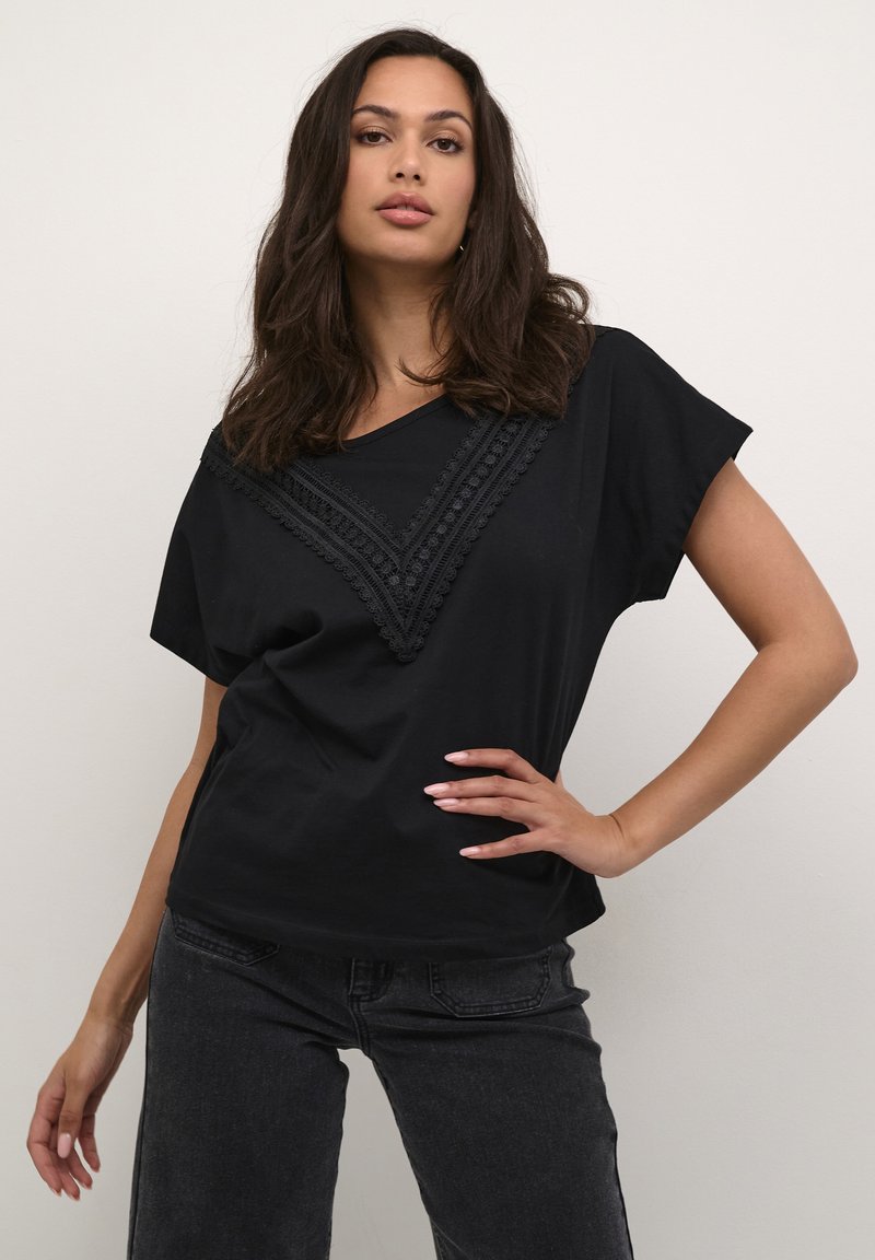 T-shirt noir à manches courtes en tissu doux, présentant un motif de dentelle texturé en V sur le devant. Coupe décontractée et sans logos visibles.