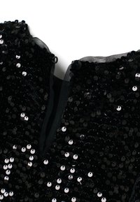 Vêtement noir pailleté avec une surface texturée, arborant un col en maille noire et une fermeture, rehaussé de paillettes rondes brillantes.