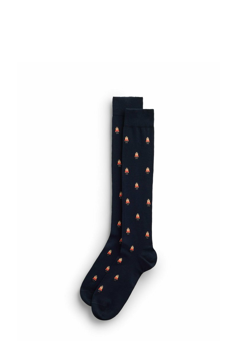 Knähöga strumpor i mörkblått tyg med ett upprepande mönster av små, tecknade figurer i klara färger. Slät textur.
