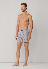 Boxer in cotone a righe con un piccolo motivo ripetuto di pinguini. Vita elastica, vestibilità ampia e lunghezza fino a metà coscia.