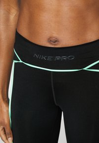 Czarne legginsy Nike Pro z szerokim pasem z wytłoczonym logo, ozdobione jasnoniebieskimi liniami po bokach. Gładki, elastyczny materiał.