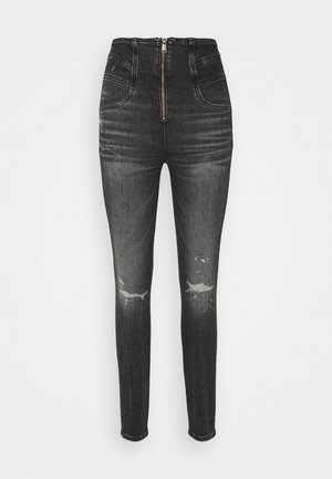 Jean en denim noir taille haute avec une fermeture éclair, présentant une coupe skinny, des détails déchirés et un léger délavage sur le tissu.