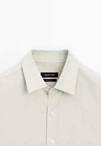 Lichtgrijze button-up overhemd met een gestructureerde kraag, gladde textuur en contrasterende witte knopen. Etiket zegt "Massimo Dutti."