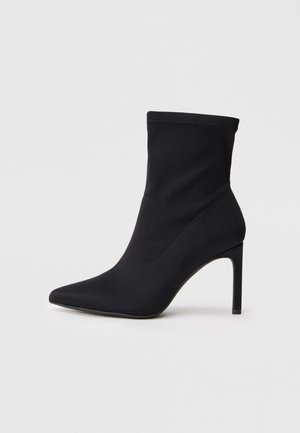 Black pointed-toe sock boot with slim high heel and stretchy fabric ankle shaft against white background.